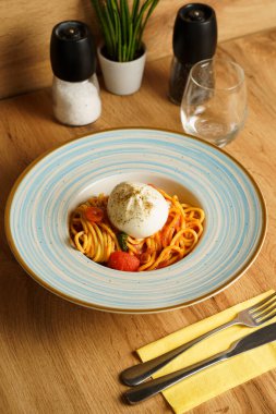 Bir burrata topuyla kaplı bir spagetti tabağı, kiraz domatesli ve fesleğenli domates sosuyla servis ediliyor. Kremalı peynir, canlı makarnayla çok güzel zıtlaşıyor..