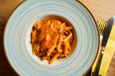 Zengin, kremalı domates sosuyla kaplanmış, mavi ve beyaz çerçeveli bir tabakta servis edilen lezzetli bir makarna tabağı. Canlı turuncu rengi rahatlatıcı ve doyurucu bir yemek olduğunu gösteriyor..