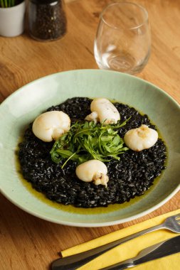 Kurutulmuş mürekkep balığı ve taze roka garnitürle kaplı siyah mürekkep balığı pilavı tabağı. Pastel yeşil seramik tabaktaki canlı yeşil ve koyu siyah kontrast..