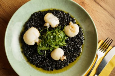 Kurutulmuş mürekkep balığı ve taze roka garnitürle kaplı siyah mürekkep balığı pilavı tabağı. Pastel yeşil seramik tabaktaki canlı yeşil ve koyu siyah kontrast..