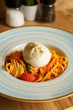 Bir burrata topuyla kaplı bir spagetti tabağı, kiraz domatesli ve fesleğenli domates sosuyla servis ediliyor. Kremalı peynir, canlı makarnayla çok güzel zıtlaşıyor..
