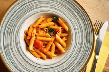 Canlı domates sosuyla kaplanmış, taze kiraz domatesleri ve fesleğen yapraklarıyla süslenmiş minimalist bir makarna servisi. Sıcak ahşap arka plan bu İtalyan yemeğinin tazeliğini vurguluyor..