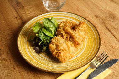 Sarı çizgili tabakta canlı karışık salata sebzeleriyle servis edilen kızarmış tavuk filetoları. Tabak, taze, yapraklı elementlerle çıtır çıtır dokuya zıt düşüyor..