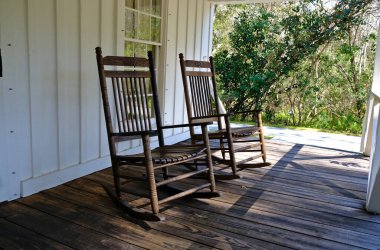 Eski tip sallanan sandalyeler arka planda ağaçlar olan Florida tarzı bir verandada oturuyorlar.