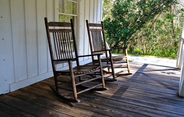 Eski tip sallanan sandalyeler arka planda ağaçlar olan Florida tarzı bir verandada oturuyorlar.