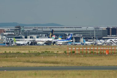 Fotoğrafta Frankfurt Havaalanı 'nda önlük sergilenirken, ön planda birkaç yolcu uçağı yer alıyor. Arka planda, terminal binası ve ikonik kontrol kulesi görünür.