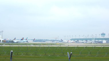 11 Ekim 2015 'te çekilen bu fotoğraf, Münih Havalimanı' ndaki apron ve terminal alanlarını geniş açıdan gösteriyor. Kapılara birkaç uçak park edilmiş durumda. Jet köprüleri ile birbirlerine bağlılar.