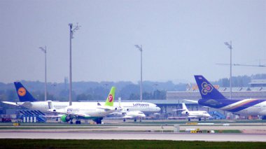 11 Ekim 2015 'te çekilen bu fotoğraf, Münih Havalimanı' ndaki apron ve terminal alanlarını geniş açıdan gösteriyor. Kapılara birkaç uçak park edilmiş durumda. Jet köprüleri ile birbirlerine bağlılar.