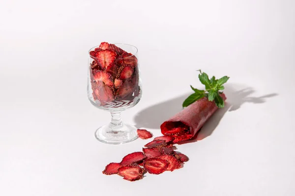 Fruit marshmallow, dried strawberry slices in a glass and strawberry pastille rolls isolated on white background. Healthy Eating. Healthy snacks. Garnished with a sprig of fresh mint. Sugar-free.