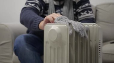 Blurred Shooting with a Man Sitting in the Sofa, on a Cold Winter Day, Putting Wool Socks and Gloves to Get Warm on a Radiator.