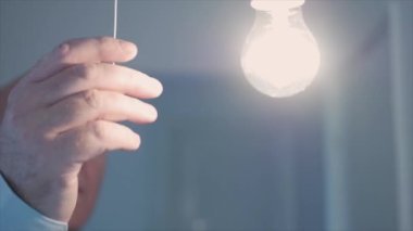 One Person Pulls the Switch Cord and Turns Off the Light in a Room. Saving Electricity and Making Economy Concept.