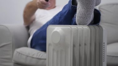 Blurred Shooting with a Man on the Sofa Using a tv remote, wearing Wool Socks on his Feet, and Getting Warm on a Radiator.