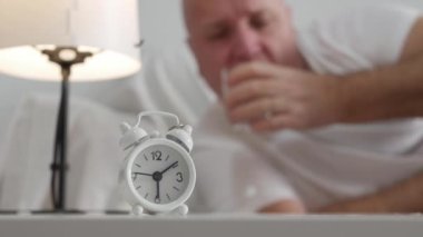 Blurred Shooting with a  Tired and Thirsty Elderly Person Taking a Sip from a Glass of Water and Lying in Bed at Home.