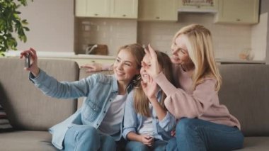 Üç kuşak. Mutlu gülümseyen büyükanne, kız ve torun evde kanepede oturup sarılıyor, selfie çekiyor ve gülümsüyor. Aile ilişkileri ve değerleri