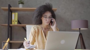 Gözlüklü Afrikalı Amerikalı bin yıllık kadın cep telefonuyla danışmanlık yapıyor. Konsantre olmuş, melez bir kadın.