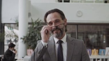 modern orta yaşlı işadamı, gözlüğünü çıkarıp kameraya gülümsüyor.