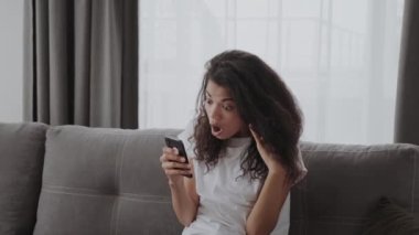 Şok olmuş genç bir kadın telefona bakıyor. Kötü haber fotoğrafları görüyor. Yüzünde korku dolu bir ifade var.