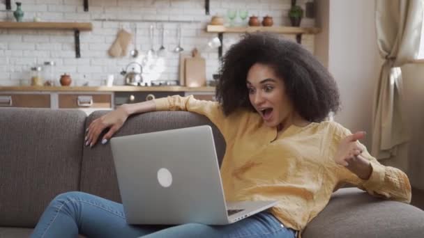 驚くべきアフリカ系アメリカ人女性は彼女のラップトップを見て非常に驚いています 隔離モード自宅でリラックス — ストック動画