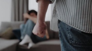 Erkek eli yakın oturduğu yerde oturan ve kendini koruyan karısını dövmeye hazır. Aile içi şiddet, saldırganlık suçu kavramı.