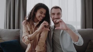 Ön planda kalp hareketi. Odak dışı, aşık bir çift kanepeye oturur ve elleriyle bir kalp hareketi gösterir. Aşk ve ilişki kavramı.