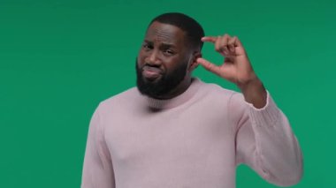 Genç Afro-Amerikan bir adam elleriyle hareket ediyor parmaklarıyla küçük boy işareti yapıyor ve kameraya bakıyor. Ölçüm. Stüdyoda yeşil arka plan üzerinde