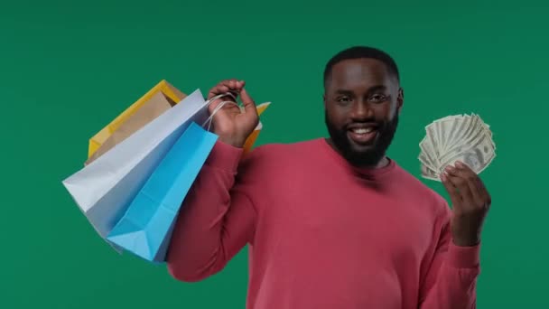 カラフルなショッピングバッグやドルを持つアフリカ系アメリカ人男性 ブラックフライデーセール ハッピーショッピング グリーンスクリーン クロマキー — ストック動画