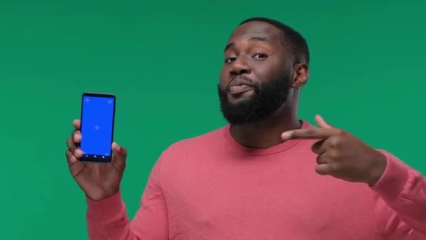 快乐的年轻黑人男子用彩色键显示他的手机屏幕 并在绿色屏幕上指向它 彩色键 — 图库视频影像