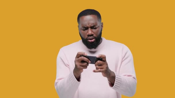 Schwarzer Junger Afrikaner Spielt Begeistert Spiel Auf Smartphone Auf Gelbem — Stockvideo