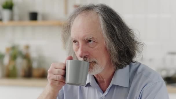 高齢者の白髪の男性は キッチンで自宅でおいしい香りのコーヒーを楽しんでいます — ストック動画