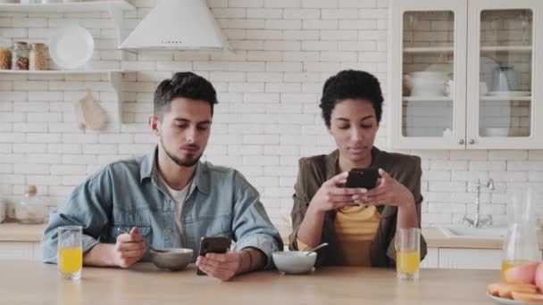 千年多种族夫妇的智能手机无视彼此在家一起吃早餐 严肃的年轻男子和非洲裔美国妇女专注于使用移动应用程序或检查社交 — 图库视频影像