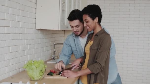 厨房里的一对年轻的多种族夫妇做沙拉 切蔬菜 互相喂食 健康食品概念 — 图库视频影像