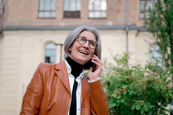 stock image Senior grey hair woman with eye glasses smiling talking on the phone standing outdoors park background with laptop in a hand