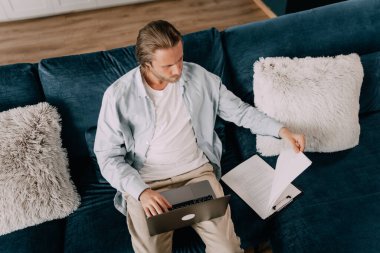 Bir çalışan uzaktan bir rapor üzerinde çalışıyor, bazı istatistiksel verilere bakıyor ve bilgisayarına bir şeyler yazıyor. Ciddi görünüyor ve evdeki bir kanepede oturmaya odaklanmış.