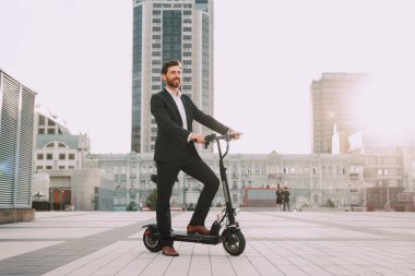 Elektrikli scooter kullanan takım elbiseli genç ve modern bir iş adamı. Ekolojik ulaşım kavramı