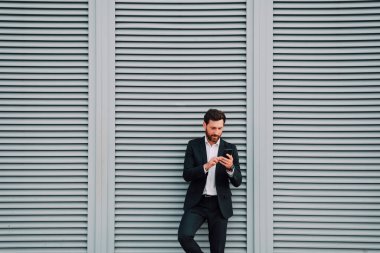 Tuğla duvar arka planında iş adamı telefon uygulaması kullanıyor. Metin için boş alan. Akıllı telefonu takım elbiseli bir iş adamı tutuyor. Kentsel genç profesyonel yaşam tarzı