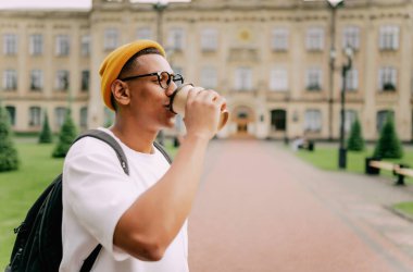 Havalı, sıradan, gülümseyen genç bir adamın portresi. Afrikalı Amerikalı öğrenci kahve içiyor ve gülümsüyor.