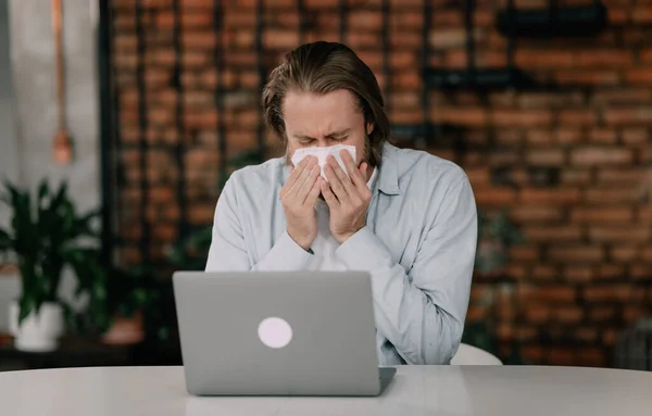 stock image sickly young man blowing his nose with a tissue.