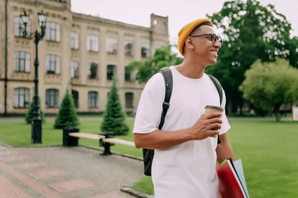 一个年轻的国际学生提着背包和咖啡杯走进校园的场景 — 图库照片
