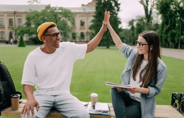 Two young people are studying together in university. Students outdoors giving five to each other