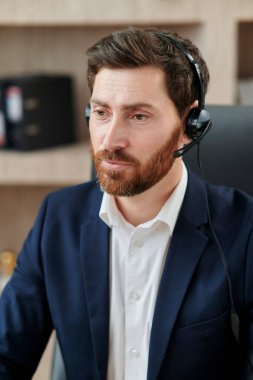 Temsilci pratisyen, takım elbise ve kulaklık giyerek, olumlu titreşimlerle, aktif jestlerle ve açıklamalarla çevrimiçi eğitim veriyor..