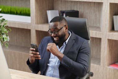 Heyecanlı mutlu Afrikalı iş adamı profesyonel kazanan başarıyı kutluyor. Akıllı telefonda iyi haberler okuyor. Cep telefonundan çok mutlu ol.