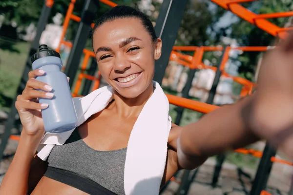 Afrikalı formda atletik kadın, güneşli bir günde spor sahasında gülümseyip selfie çekiyor..