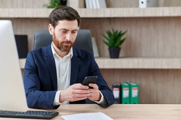İşadamı ofisinde akıllı telefonuna bir mesaj yazıyor. Takım elbise giymiş, modern ofiste çalışıyor..