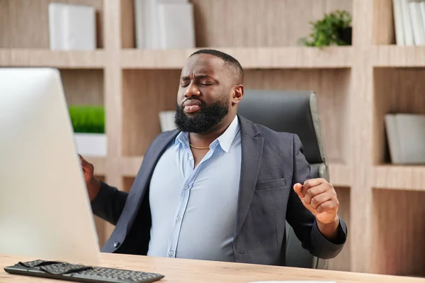 African American in business suit office worker gets uncomfortable in his office chair and sour back muscles.