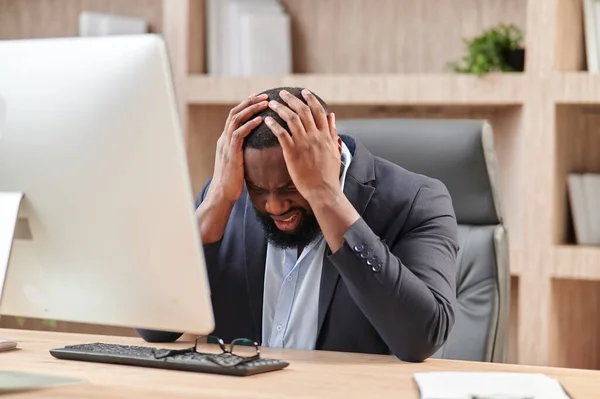 Stressful Job. Stressed African Businessman At Worckplace Touching Head Having Problem At Workplace Sitting In Modern Office. Crisis And Entrepreneurship Business Issues, Headache Concept
