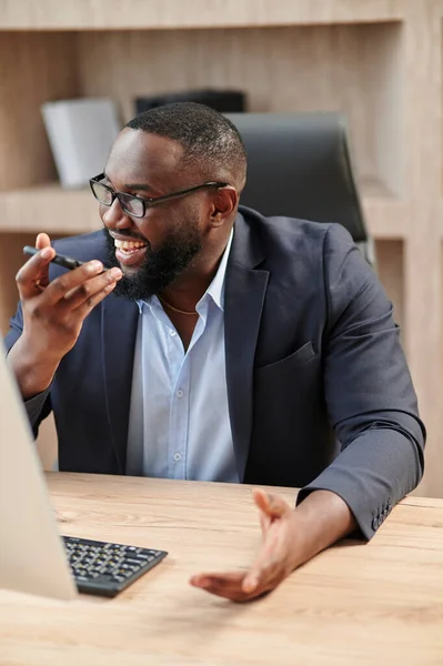 African American Businessman seated at workplace sending voice message, solving issues distantly. Business, instant communication, modern tech easy usage concept