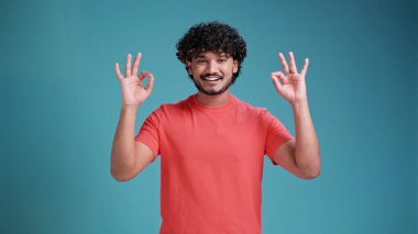 Her şey yolunda, olumlu adam tamam işareti gösteriyor. Fotoğrafı kapat. Jest konsepti, temel mercan tişörtü içinde mavi stüdyo arka planında izole edilmiş..