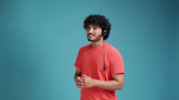 ブルースタジオの背景にサンゴのTシャツで話して頭セットとインドの男性コールセンターオペレーター — ストック写真