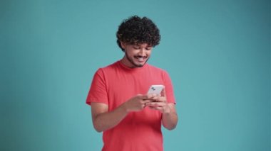 20 'li yaşlardaki harika, eğlenceli Latin bir genç. Cep telefonu kullanıyor, daktilo yazıyor, sohbet ediyor. Mavi stüdyo arka plan stüdyosuna mesaj gönderiyor..