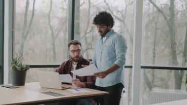 Bir ofiste iki etnik çeşitlilikte çalışan ellerinde belgelerle finans raporunu tartışıyor. Latin ve Avrupalı erkekler ortak çalışma alanında bir projeyi tartışıyor.